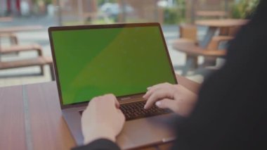 NEW YORK - 5 Eylül 2020: Laptop bilgisayarında oturan, yeşil ekrana bakan, klavyede yazan siyah takım elbiseli genç iş kadınını vurmak. Tanımlanamayan halkla ilişkiler yöneticisi dışarıda çalışıyor.