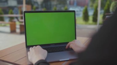 NEW YORK - 5 Eylül 2020: Kafe 'de yuvarlak tahta masada gümüş dizüstü bilgisayar kullanarak oturan genç serbest çalışanın görüntüsü. Klavyede yazan siyah takım elbiseli kız mesajlara cevap veriyor. Bulanık