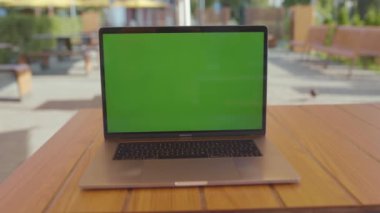 NEW YORK - 5 Eylül 2020: Kafe terasındaki yuvarlak ahşap masada izole edilmiş yeni gümüş dizüstü bilgisayarın yakın çekim görüntüleri. Yeşil ekranlı taşınabilir bilgisayar görüntüsü. Şehir, hiç kimse. İnsanlar olmadan