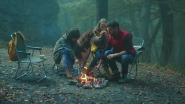Köpekli bir aile, sonbahar akşamı ormanda kamp ateşinin etrafında oturur. Ormandaki bir yangında sosis kızartmak. Arkadaşlık şömineyi pişirir. Kapatın. Yavaş çekim