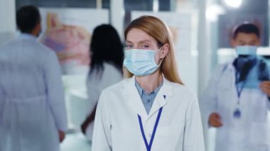 Karantinada virüs koruyucu maske takarak kameraya güvenerek kollarını kavuşturan beyaz, genç, yetişkin doktor doktor doktor doktor doktor. Portreler.