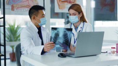 Asyalı terapist kadın pratisyen doktorla konuşuyor. Hastalık belirtilerini tartışıyor. Akciğer enfeksiyonu ve röntgen fotoğrafı. Tıbbi çift. Hastaneler.