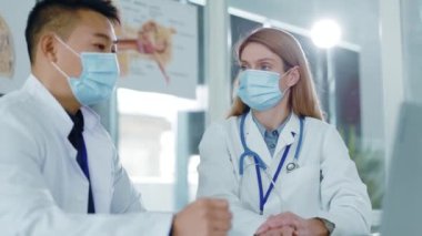 Çok ırklı bir çift doktor ve hemşire koruyucu maskeler takıp hastane sağlık bürosunda hastalık ve tedavi teşhislerini tartışıyorlar..