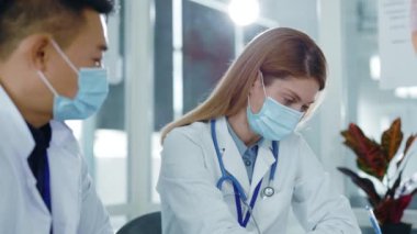 Çeşitli çok kültürlü Asyalı başhekim ve Kafkas hemşire maske takıp hasta hastalıklarını tartışıyorlar. Sağlık çalışanları. Hastane personeli.