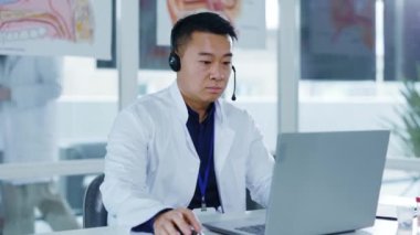 Kulaklık takan Asyalı genel pratisyen doktor hastane ofisindeki hasta ile bilgisayar kamerası görüntülü sohbet konferansı aracılığıyla konuşuyor..