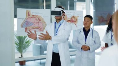 VR kulaklık takan başarılı beyaz doktor tıbbi çok ırklı personele yeni teknolojiler sunuyor ofis hastanesinde işbirliği yapan 3D cihaz projesi.