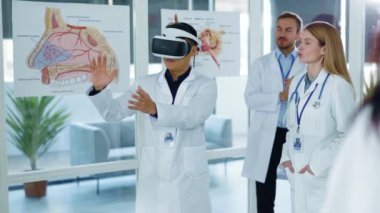 Artırılmış gerçeklik. Hastaneler. Sanal gerçeklik kulaklığı takan Asyalı başhekimi alkışlayan çok ırklı personel, tıp ofisinde modern sunum hologramını gösteriyor..