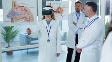 VR teknolojilerini test eden çok kültürlü tıbbi personel, hastane ofisinde gelecekte holografik sunum yapacak olan kadın çalışanlara kulaklık takıyor. Personel alkışlıyor..