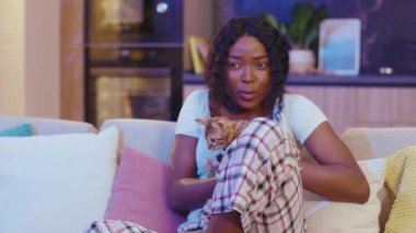 Oturma odasındaki kanepede oturan korkmuş Afrikalı Amerikalı kadın. Geceleri televizyon izlerken uzaktan kumandayla kanal değiştirmek. Yavaş çekim
