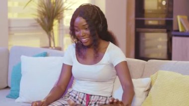 Kedili Afro-Amerikan kadın kulaklık takıyor iletişim kurarken dizüstü bilgisayar kullanıyor. Evde video var. Mesafe ilişkisi. Gülümsüyor. Yavaş çekim
