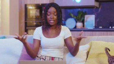 Kedi sohbeti yapan, gülümseyen Afro-Amerikan kadın dizüstü bilgisayar kullanıyor. Evde video var. Mesafe ilişkisi. Yavaş çekim