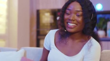 Gülen suratlı, kulaklıklı, iletişim kuran, bilgisayar kullanan Afro-Amerikan kadın. Evde video var. Mesafe ilişkisi. Yavaş çekim