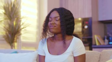 Genç Afro-Amerikan genç bayan kameranın başparmağına bak. Oturduğu koltukta oturuyor. Karantina zamanı. Evde kal. Kapatın. Yavaş çekim