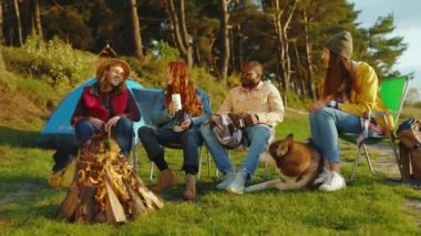 Mutlu arkadaşlar doğada kamp ateşiyle piknik yaparlar. Gençler oyunlar hakkında konuşurken köpek gülümsüyor. Tatil turizmi macerası. Yavaş çekim