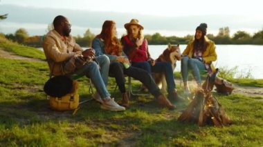 Doğada kamp ateşinin yanında oturan şık arkadaşlar. Gençler oyunlar hakkında konuşurlar, köpeklerin gülümsemesiyle mutlu olurlar. Tatil turizmi macerası. Yavaş çekim