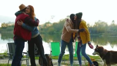 Havalı hippi arkadaşlar göl kenarında diğer insanların altında tanışmışlar. Dört genç, köpekle gülümseyen birine sarılır. Tatil turizmi macerası. Kapatın. Yavaş çekim