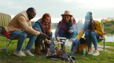 Hippiler kamp ateşinin etrafında oturur ve renkli şekerlemeleri kızartırlar. Ormandaki gençler. Kamp yapmak. Piknik. Yavaş çekim