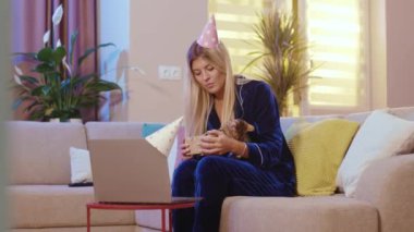 Sarışın, parti şapkalı güzel kız Bengal kedisiyle online doğum günü kutlaması eğlenceli video konferansı hediyeleri açıyor. Ev tatili. Aile ve evcil hayvanlar.