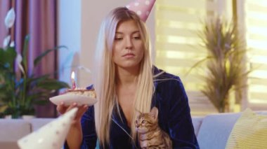 Yalnız, sefil, tatil şapkası takan, Bengal kedisi ve doğum günü pastasıyla evde tek başına kutlama yapan sarışın kadın. Yalnızlık ve duygular.