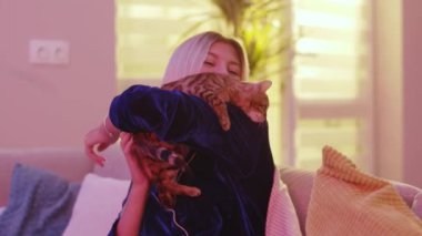 Sarışın, beyaz, mavi pijamalı bir kadın evde sevimli kedi yavrusuyla oynuyor. Anneciğinden kaçmaya çalışan eğlenceli, eğlenceli, bengal kedisi. Evcil hayvanlar. Sevimli hayvanlar..