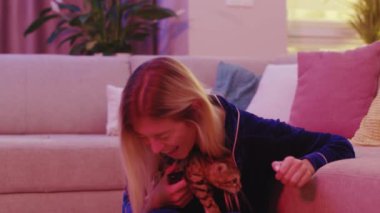 Güzel, mutlu, sarışın bir kadın televizyon programı komedi filmi izlerken kahkahalarla gülüyor Bengal kedisini okşuyor ve birlikte eğleniyorlar. Evcil hayvanlar.