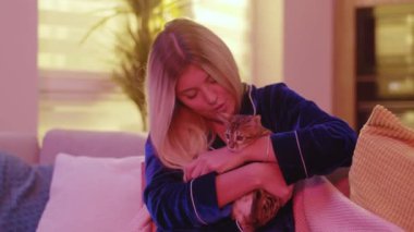 Sarışın, pijamalı güzel bir kadın sevimli Bengal kedisiyle evde zencefilli kedi oynuyordu. Evcil hayvan konsepti. Hayvanlar. Sıradan bir yaşam tarzı. Aşk konsepti.