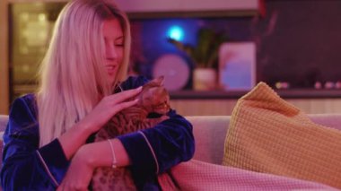 Duygusal olarak mutlu, sakin, sarışın bir kadın evde oturup güzel kızıl bengal kedisini okşamaktan zevk alıyor. Evcil hayvanlar. Evcil hayvanları olan aile.