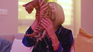 Mutlu öforik sarışın beyaz kadın pijama giyiyor kedi okşama ve sevimli tekir kedicik yavrusuyla parti yapıyor. Aileler. Hayret verici hayvan konsepti.