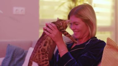 Neşeli, mutlu, mutlu, mutlu, sarışın kadın Bengal kedisine sarılıyor ve öpüyor. Sevgi dolu anları paylaşıyor, aile kavramının tadını çıkarıyor. Çekici kız ve kızıl kedi.