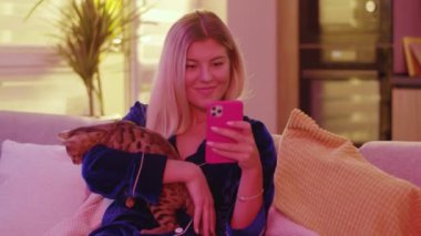 Güzel bir kadın cep telefonu sosyal medya zaman çizelgesini kullanarak tekir Bengal kedisini tutuyor evde kalan mesajları paylaşıyor. Sıradan bir yaşam tarzı. Teknoloji.