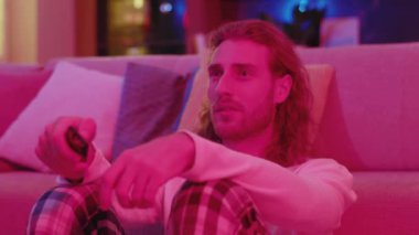 Neon ışıklarıyla televizyon izleyen neşeli, beyaz saçlı adam stand-up 'ın keyfini çıkarıyor favori komedi savaşları dizileri evde kanalı değiştiriyor..