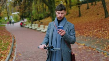 Sonbahar parkındaki hasta, genç ve şık adam elektrikli scooterla öksürüp duruyor. Ekolojik ulaşım. Virüs hastalığına alerjim var. Portre ağrısı yorucu. Kapatın. Yavaş çekim