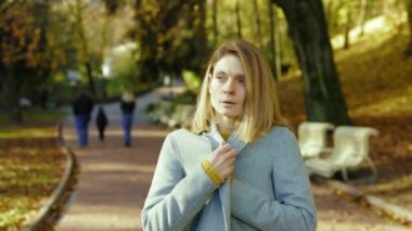 Kadın hasta, üşümüş, öksürüyor sonbahar parkında güneş ışığında etrafa bakıyor. Sarışın, stresli bayan. Portre ağrısı yorucu. Hastasın. Kapatın. Yavaş çekim