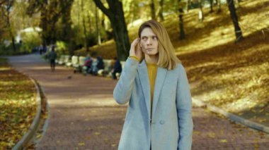 Hasta ve başı ağrıyan genç bir kadın güneş ışığında sonbahar parkında soğuk öksürük hisseder. Sarışın, stresli bayan. Portre ağrısı yorucu. Kapatın. Yavaş çekim