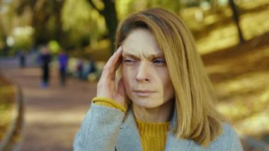 Hasta, başı ağrıyan genç bir kadın soğuk öksürük hisseder sonbahar parkında güneş ışığında kameraya bakar. Sarışın, stresli bayan. Portre ağrısı yorucu. Kapatın. Yavaş çekim