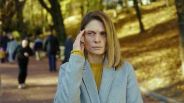 Güzel yüzü olan, mavi gözlü, başı ağrıyan soğuk hapşırıkları hisseden genç bir kadın sonbahar parkında gün ışığında kameraya bakıyor. Sarışın, stresli bayan. Portre ağrısı yorucu. Kapatın. Yavaş çekim
