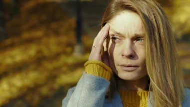 Yüzünü kapat, hasta genç kadın baş ağrısı çekiyor, hapşırıyor sonbahar parkında güneş ışığı altında kameraya bak. Sarışın, stresli bayan. Portre ağrısı yorucu. Yavaş çekim