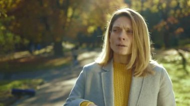 Sarışın genç bir kadın yürürken soğuk hapşırıkları hisseder sonbahar parkında gün ışığında yürürken. Ateş ağrısı, sağlıksız öksürük hastalığı, alerji. Kapatın. Yavaş çekim