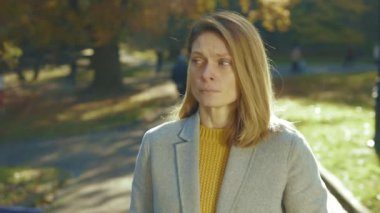 Üzgün genç kadın kameraya bakıyor. Sonbahar parkında gün ışığında yorgun ve üzgün. Ateş ağrısı, sağlıksız öksürük hastalığı, alerji. Kapatın. Yavaş çekim