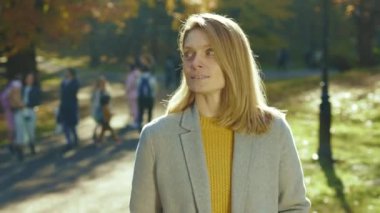 Gülümseyen genç kadın güz parkında gün ışığında öksürük içinde etrafa bakıyor. Ateş ağrısı, sağlıksız öksürük hastalığı, alerji. Kapatın. Yavaş çekim