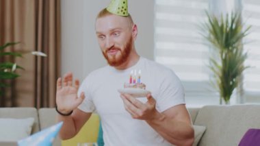 Çekici bir adam evdeki kanepede oturmuş gülümsüyor dizüstü bilgisayarla pastadaki mumları üflüyor. Karantina sırasında online video görüşmesinde doğum gününü kutluyoruz. İletişim. Kapatın. Yavaş çekim