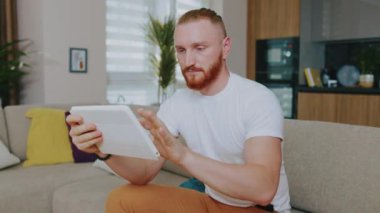 Tablet bilgisayar kullanan yakışıklı adamın yüzünü kapat. Odaklandım. Evdeki kanepede oturmak. Çevrimiçi teknoloji cihazı iletişim karantinası. Yavaş çekim