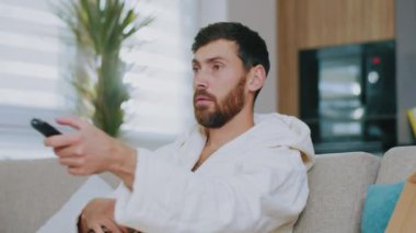 Kedili mutlu genç adam TV izlerken pizza yiyor. Evdeki kanepede oturmak. Dinlenme sinema kanalları dinleniyor. Portre. Kapatın. Yavaş çekim.