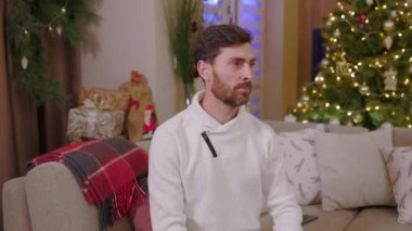 Kışın süveter giyen, gülümseyen ve kameraya gülümseyen genç adamın portresi Noel arkaplanında mutlu hisset. Yeni yıl kış tatili. Kutlama yapıyoruz. Mutlu noeller. Yavaş çekim