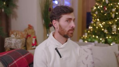 Kışın süveter giyen genç yakışıklı adam Noel arkaplanındaki kamera omuz silkiyor. Yeni yıl kış tatili. Kutlama yapıyoruz. Mutlu noeller. Yavaş çekim