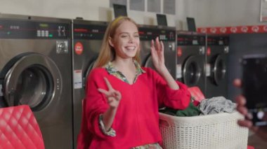 Kapalı ellerde telefon var. Arka planda sarışın bir kadın var. Çamaşır odasında oturmuş müzik pozları dinliyor. Ev işi çamaşır makinesi kurutma makinesi içeride. Kapatın. Yavaş çekim