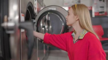 Genç sarışın kadın çamaşırlarını çamaşır sepetinden çamaşır makinesine çıkarıyor. Ev hanımı ev işi, ev işi, ev içi çamaşır yıkama rutini. Yavaş çekim