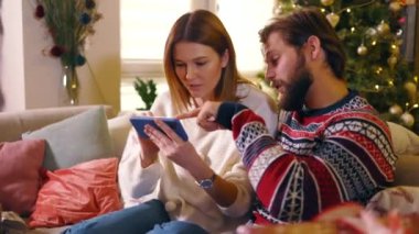 Sevecen genç çift, Noel tatiline hazırlanıyor. İnternetten hediye seçiyor. E-ticaret uygulaması, akıllı telefon..