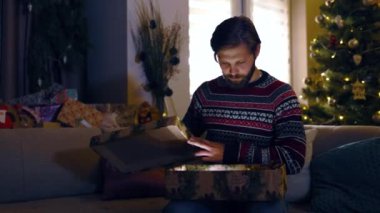 Sakallı adam kutsal gecede Noel kutusunu açıyor. Karanlık odada sihirli ışıklarla muhteşem bir hediye veriyor. Tatil atmosferi. Duygular.