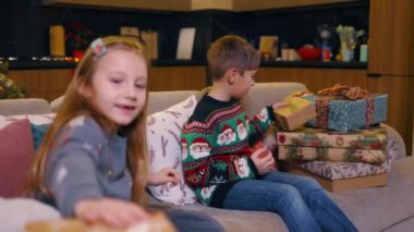 Neşeli bir çift şirin çocuk evde hediye kutularıyla oynuyorlar aile üyeleri için bayram hediyeleri paketliyorlar. Çocukluk. Heyecan, duygular. Noel.
